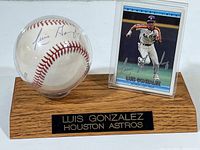 Baseball signed by Luis Gonzalez in clear protective case on wooden display stand, with a Luis Gonzalez baseball card behind the stand.