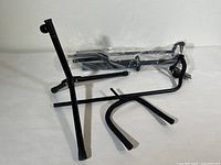 Photo showing black metal guitar stand parts disassembled on a white surface. Included are tripod base, vertical support arm, and U-shaped yoke for cradling guitar neck.