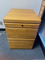 Photo of light wood 2-drawer filing cabinet with black knob on top drawer lock and smooth finish on a carpeted floor.