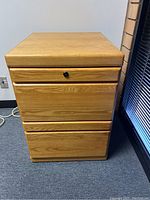 Front view of a 2-drawer wooden filing cabinet showing the light oak wood finish, top drawer with black knob, and larger bottom drawer.