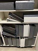 Shelves with an assortment of black, white, and grey 3 ring and 3-D ring binders in various sizes.