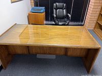 Front angle view of the solid wood desk showing the transparent glass top panel and the wood grain surface below. Desk dimensions visible in room context.