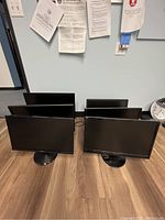 Photo showing six desktop monitors arranged in two rows on a wood floor with various brand logos visible on backs and stands.