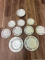 Overview photo showing two dinner plates, four salad plates, three saucers, and one bowl arranged on floor, all with matching English Garden 225 floral rim design.
