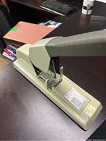 Heavy duty stapler shown open on a dark desk with visible handle and loading area