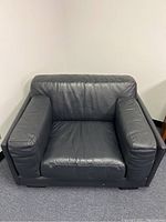 Front view of the black leather chair showing padded armrests, seat cushion, and backrest.