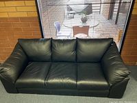 Front view of the black leather sofa placed against a brick wall with window behind.