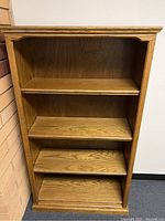 Front view of wooden bookcase showing 4 shelves with a medium oak finish and visible wood grain.