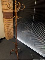 Full view of the wooden spinning coat rack showing its spiral central spindle, curved hooks, and tripod base.