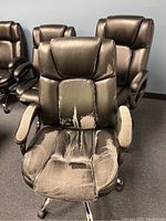 Close-up of a large black leather conference chair with significant peeling and wear on seat and backrest, padded armrests showing fabric wear.