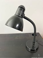 Photo showing the black desk lamp with a bendable neck and round base on a desk, lamp bulb off.