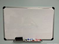 Front view of the rectangular dry erase board with attached bottom tray holding two black erasers and eight colored dry erase markers.