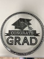 Photo of one graduation paper plate showing design with a graduation cap and 'Congrats Grad' text in black and white.