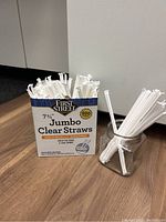 Photo showing box of First Street 7 3/4 inch Jumbo Clear Straws labeled 500 count with individually wrapped straws inside and a clear glass jar containing some straws
