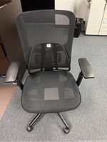 Front view of black mesh task chair showing seat, removable lower backrest, adjustable armrests, and wheeled base.