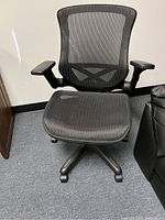 Front view of black mesh office desk chair showing mesh seat and backrest, raised armrests, and five-legged base with casters.
