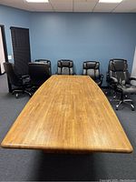 Large oak conference table with visible wood grain and rounded edges, with black leather office chairs behind it