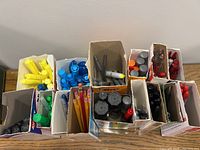 Top view of multiple compartments containing pens, pencils, highlighters, and markers in colors red, blue, orange, yellow, green, and black, arranged in cardboard holders on a wooden surface.