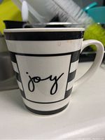 Side view of the porcelain coffee mug showing black and white stripes and the word "joy" in script on one side with some coffee stains near the rim.