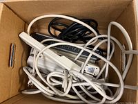 Box containing eight assorted power strips in white and black with cords tangled together.