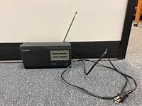 Photo of Sony ICF-24AC radio showing front controls, speaker, antenna extended, and attached power cord.