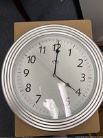 Top-down photo of white and silver wall clock showing clear view of clock face, numbers from 1 to 12, and clock hands.
