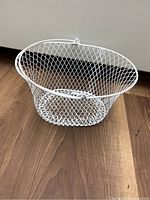White wire basket on wooden floor showing shape, mesh design and handle
