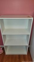 Front view of white bookcase showing three shelves and overall rectangular shape.