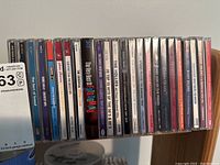 Row of various used music CDs with titles visible including Journey, U2, Queen, The Beatles, and others.