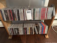 Two wooden shelves holding a collection of assorted music CDs in jewel cases arranged in two rows.