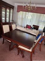 Photo of dining table with 6 chairs stacked and arranged around it in a room with a chandelier and window.