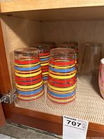 Clear glasses with multi-colored horizontal stripes inside wooden cabinet shelf.