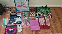 Photo showing 11 different reusable bags laid out on the floor, various sizes and flamingo-themed designs, some tropical and some with hearts or classic black and white photo prints.