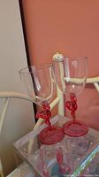 Two clear wine glasses with pink flamingo stems and bases on a reflective surface.