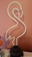 White neon-style flamingo shaped light on black base photographed against a pink wall.