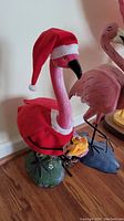 Photo of fabric flamingo statue wearing Santa hat and jacket standing on decorative base with small accessories