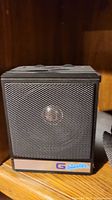 Photo of a black G Blaster speaker with grille showing and logo plate on the front.
