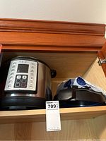 Photo of Yedi rice cooker and owner's manual beside two cookbooks in a wooden cabinet.