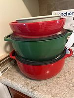 Stacked red and green cast iron pots with handles topped by ceramic bowls.