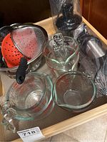 Overview of kitchen items including glass measuring cups, colanders and hand blender wrapped in plastic.