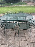 Full view of green wrought iron oval dining table with four dining chairs visible around it.