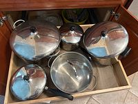 Five stainless steel pots with lids arranged in a kitchen drawer showing the top view.