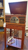 Front view of Crosley record player with wooden stand, showing the speaker grill and control panel under the hinged lid.