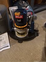 Photo showing Ryobi 1.5 HP Peak router with handles and power cord, placed on the floor.