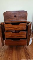 Table showing open side doors revealing three wooden drawers inside