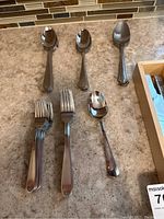 Silverware pieces including spoons, forks, and knives laid out on a countertop showing a polished stainless steel finish.