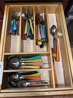 Top-down view of entire silverware set in wooden drawer organizer, showing forks, knives, tablespoons, and smaller spoons with colorful plastic handles.