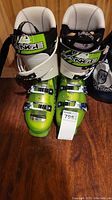 Pair of green and white Völkl V-Range sledding boots with buckles on wooden floor