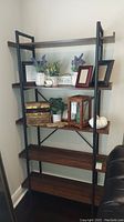 Side front view of the 5-tier metal and faux wood bookcase decorated with plants, photo frames, and decorative objects.