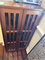 Front view of medium brown wood storage cabinet with glass panels and vertical wooden slats.